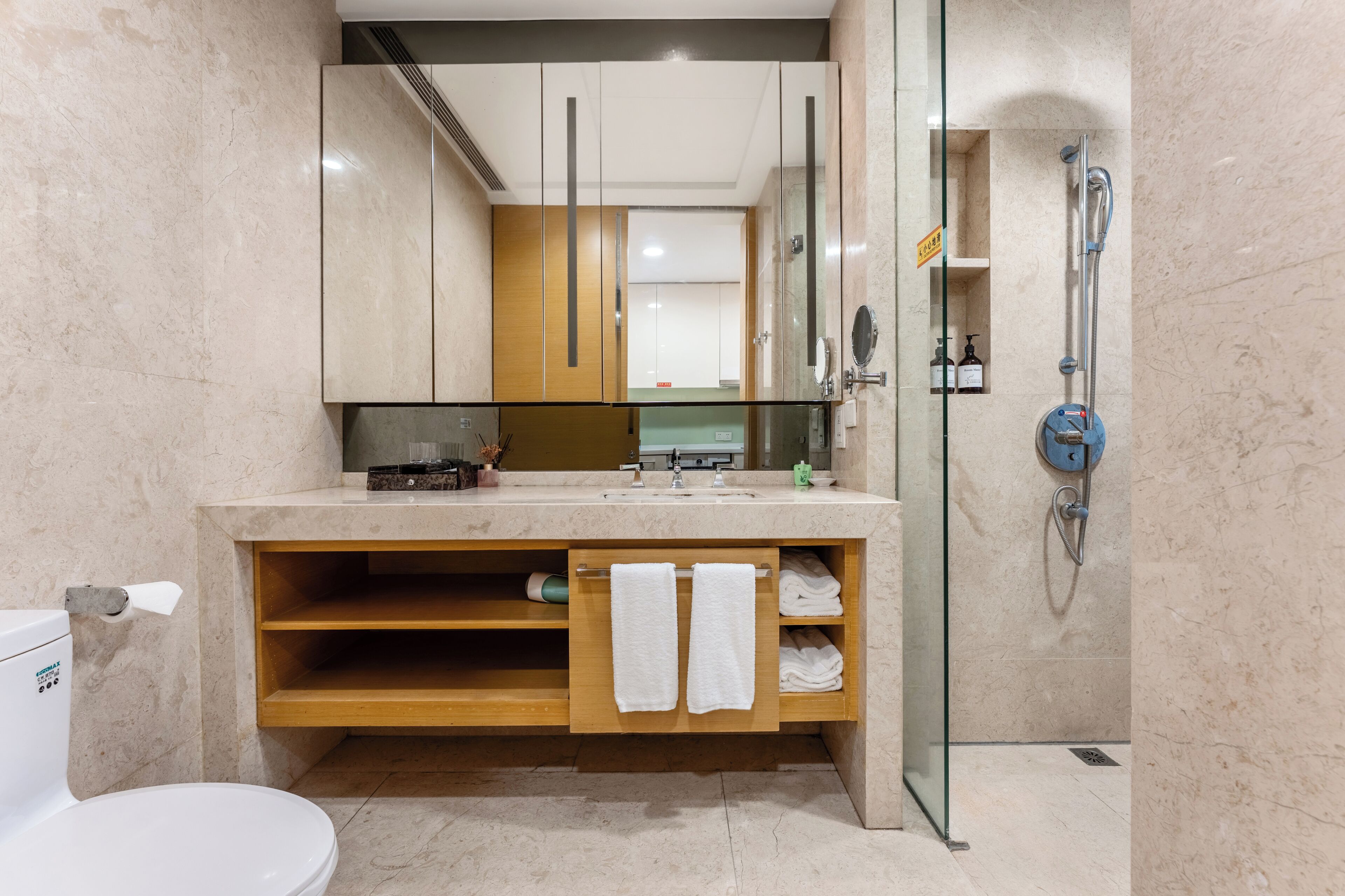 A modern bathroom with a glass-enclosed shower, a marble sink, and a wooden vanity with towels.