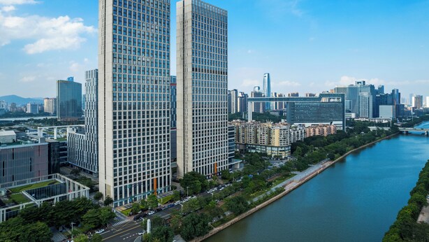A high-rise building with a grid-like facade, surrounded by other modern buildings and a river. - Side Apartment (Guangzhou)