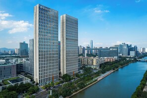 A high-rise building with a grid-like facade, surrounded by other modern buildings and a river. - Side Apartment (Guangzhou)