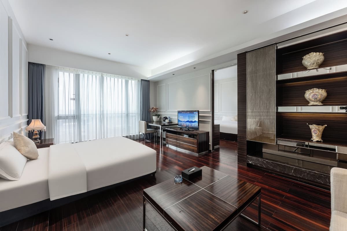 A modern hotel room with a large bed, a TV, a desk, and a decorative shelf.