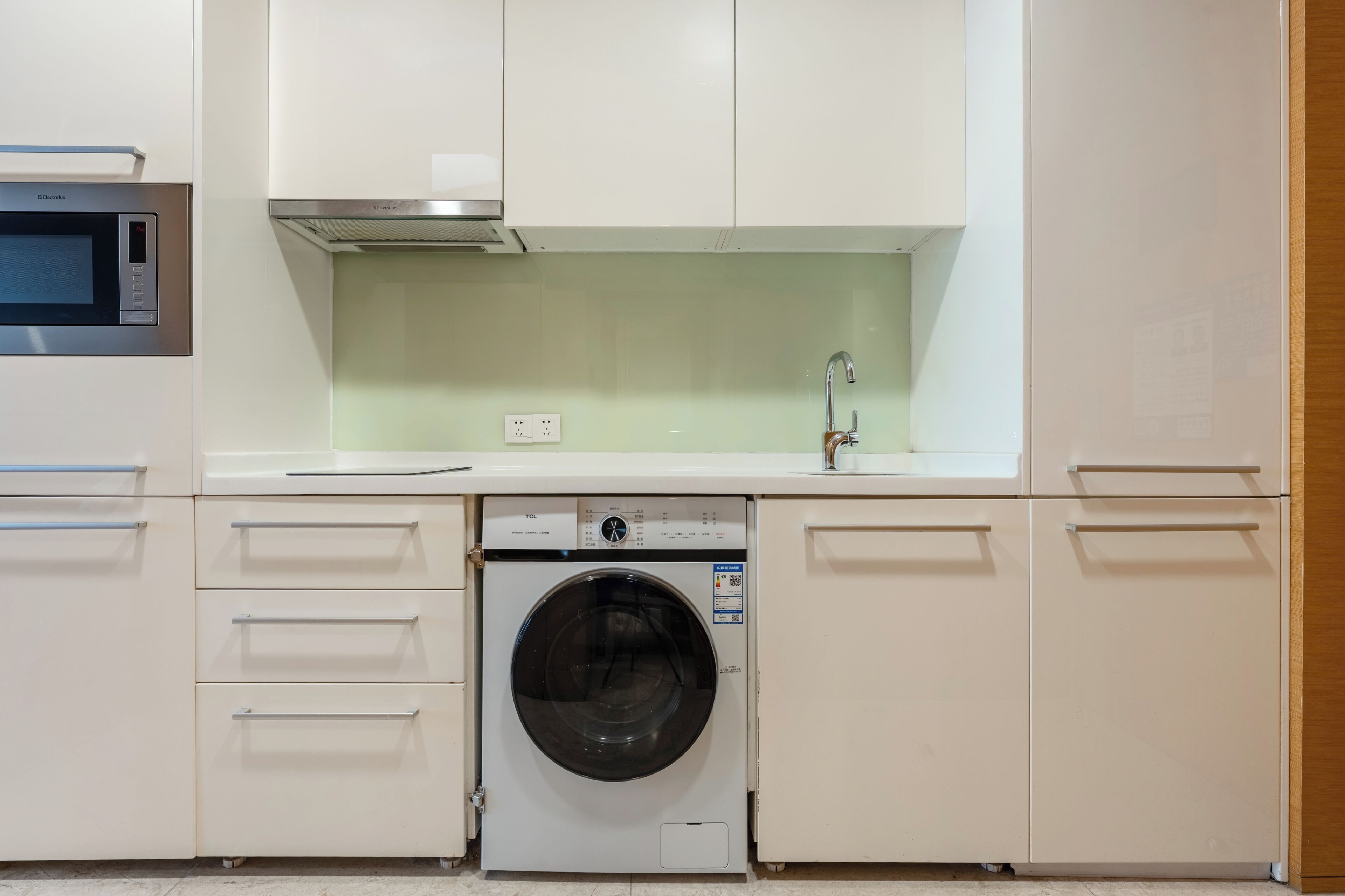 Une cuisine compacte équipée d’un lave-linge, d’un four à micro-ondes et d’un évier avec un robinet.