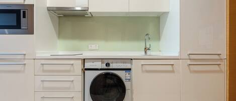 Une cuisine compacte équipée d’un lave-linge, d’un four à micro-ondes et d’un évier avec un robinet.