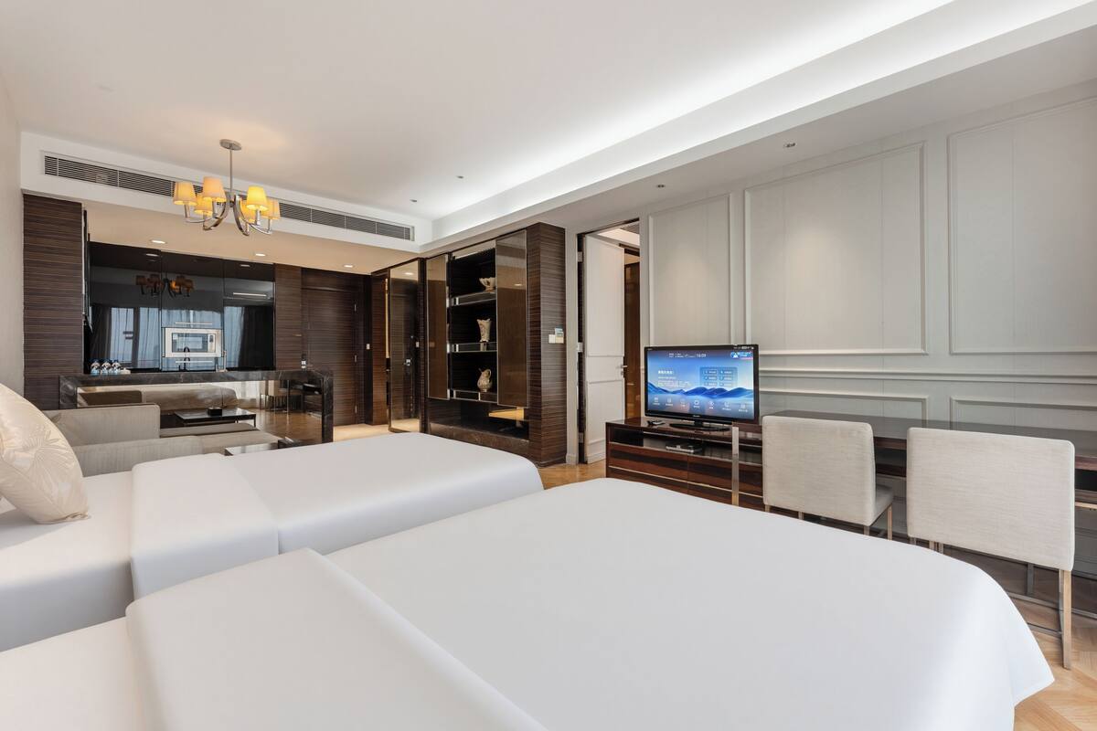 A hotel room with two beds, a TV, a dining area, and a kitchenette.
