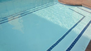 Ein klares Schwimmbecken mit blauen Bahnteilern und einem Beckenrand aus Ziegelsteinen.