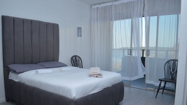 Ein modernes Schlafzimmer mit einem großen Bett, einem Sessel und einem Balkon mit transparenten Vorhängen.