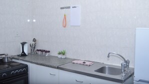 Eine Küche mit weißen Schränken, einer Edelstahlspüle, einem Herd und einer Arbeitsplatte mit verschiedenen Gegenständen, darunter ein Wasserkocher, eine Pflanze und ein Schneidebrett.