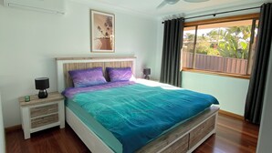 A bedroom with a bed, nightstands, a ceiling fan, a window with curtains, and a view of greenery outside. - The Rocks Family entertainer, just 10-min walk to town & beach! (South West Rocks)