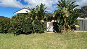 A residential property with a house, a well-maintained lawn, and large banana trees. - The Rocks Family entertainer, just 10-min walk to town & beach! (South West Rocks)
