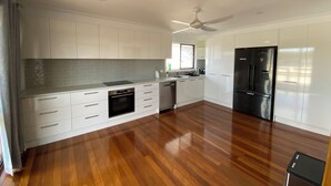A modern kitchen with white cabinets, a black refrigerator, and a wooden floor. - The Rocks Family entertainer, just 10-min walk to town & beach! (South West Rocks)