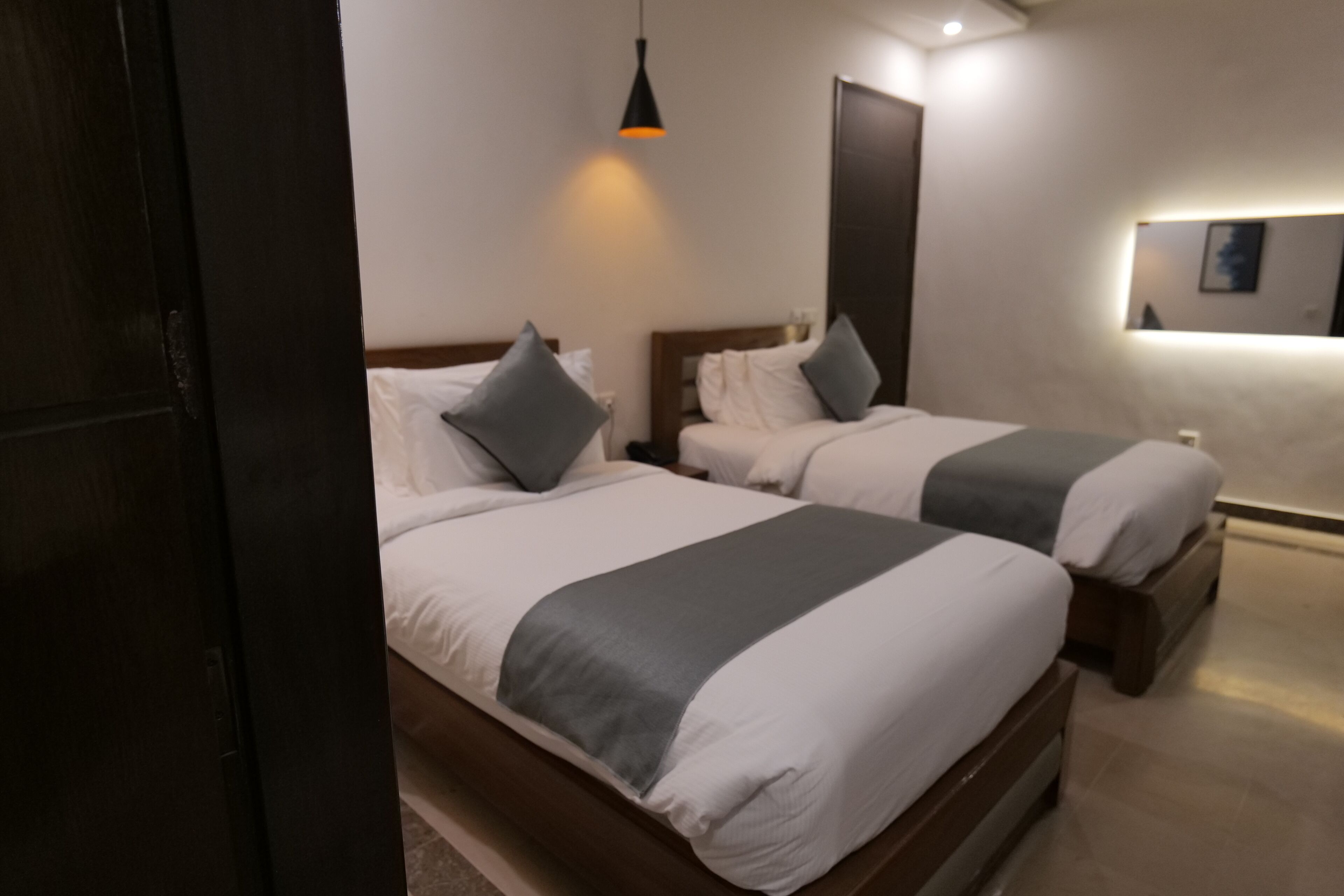 Habitación de hotel con dos camas, cada una con cabecero de madera, ropa de cama blanca y almohadones grises. En cada cama hay una mesita de noche con una lámpara.
