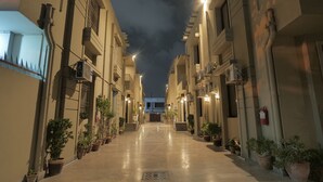 Une ruelle étroite et bien éclairée, bordée d’immeubles ornés de plantes en pot.