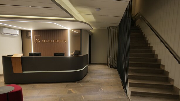 Un hall d’hôtel avec un comptoir d’accueil incurvé, un mur recouvert de panneaux en bois et un escalier situé sur la droite.