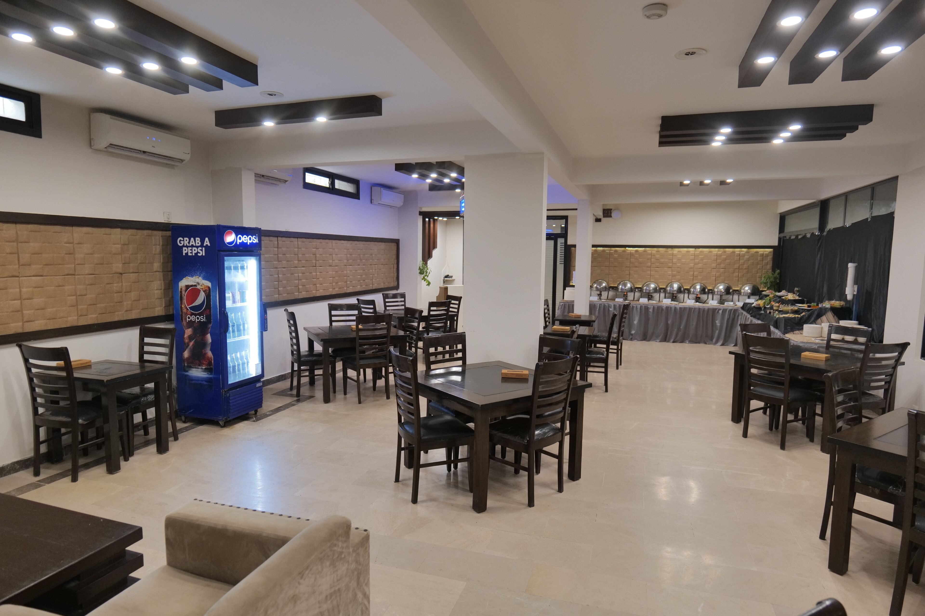A restaurant with multiple tables and chairs, a Pepsi refrigerator, and a wall-mounted air conditioning unit.
