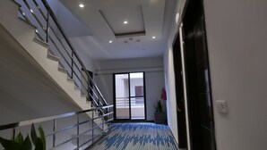 Un hall d’hôtel moderne avec un escalier, une moquette à motifs et une grande porte-fenêtre coulissante donnant sur un balcon.