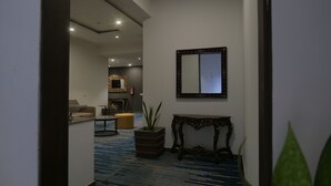 Un hall d’hôtel avec un tapis bleu, un miroir, une plante en pot et une petite table.