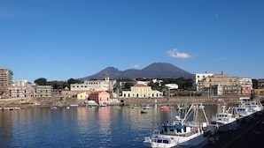 A coastal town with a marina, buildings, and a mountain in the background. - Mini Apartment With Bathroom and Kitchen (Portici)