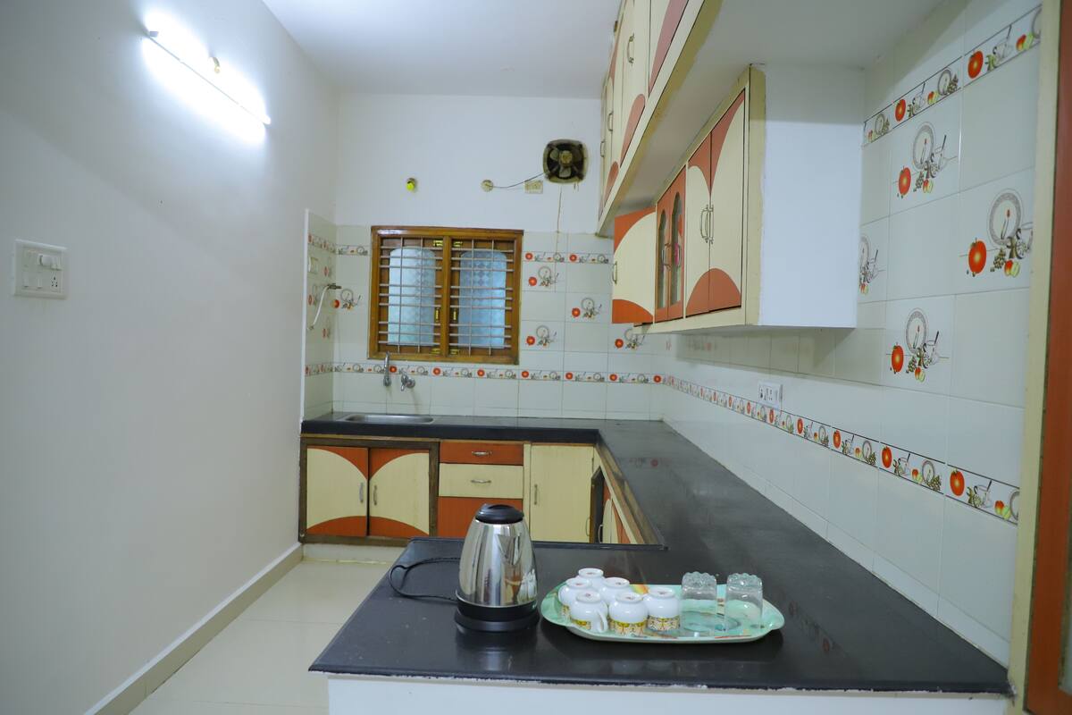 Cozinha com bancada preta, chaleira e um prato com xícaras.