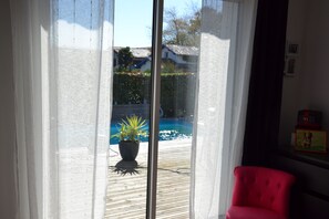 A room with a sliding glass door leading to a wooden deck with a potted plant and a swimming pool. - Confortable Maison Avec Piscine , Proche du Centre de Bayonne, Animaux Acceptés! (Bayonne)