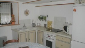 Una cocina compacta con un lavamanos, estufa, microondas y un refrigerador pequeño. Hay una mesa de comedor con un libro encima.
