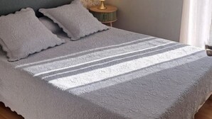 Una cama con una colcha texturizada, una lámpara de noche y un papel tapiz floral.