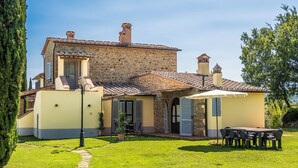 Un bâtiment en pierre avec un toit en tuiles, une terrasse dallée et un petit jardin.