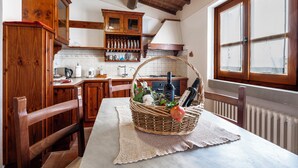 Une cuisine avec des meubles de rangement en bois, une table à manger avec un set de table et un panier contenant des bouteilles et des plantes.