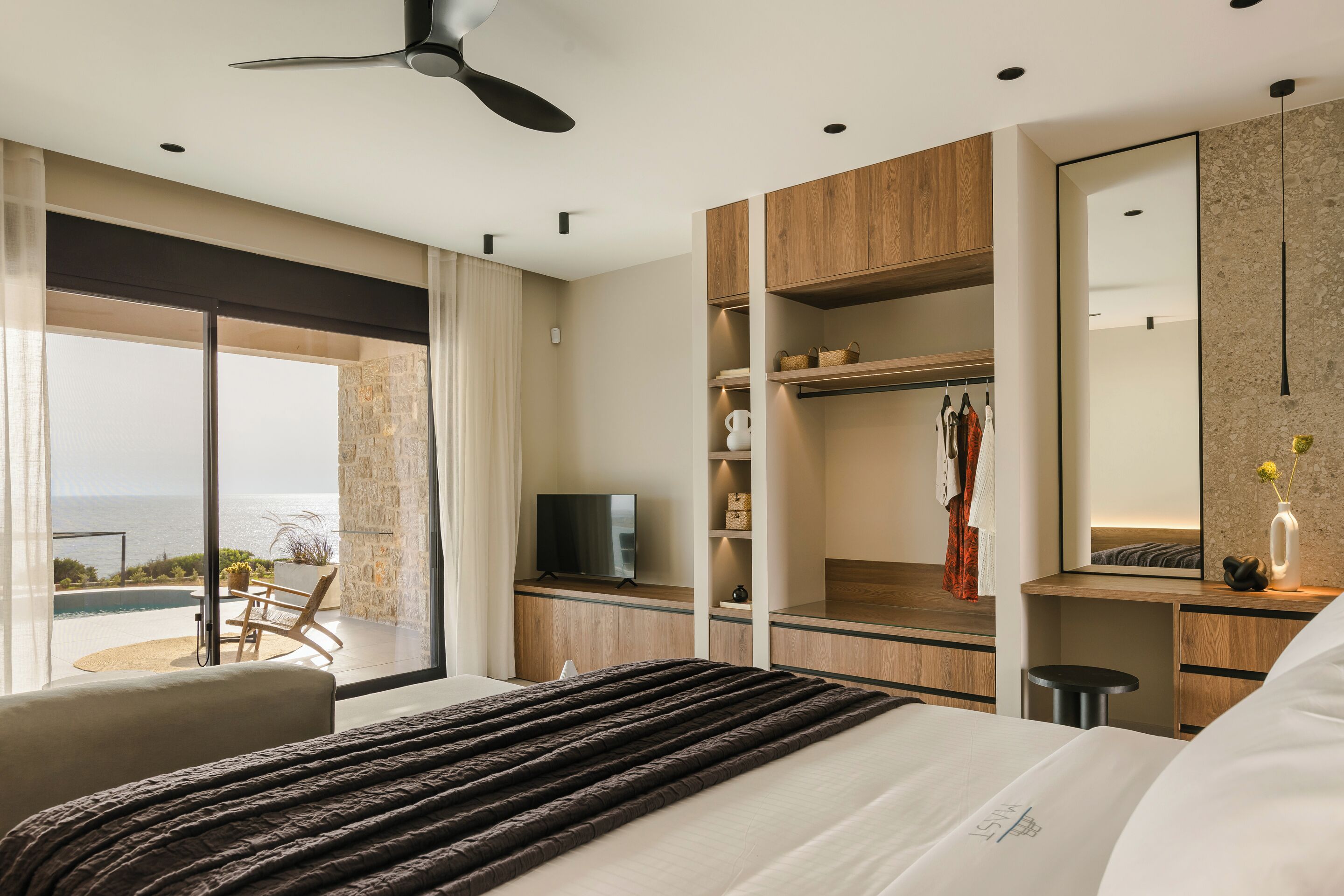 Una habitación de hotel moderna con una cama grande, televisión, armario y balcón con vistas al mar.