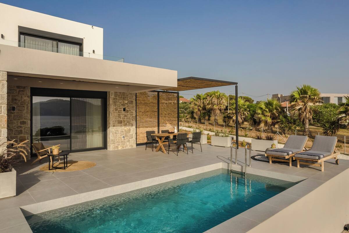 A modern outdoor pool area with a stone wall, a glass door entrance, and a seating area with a table and chairs.