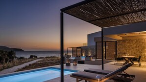 Zona de piscina moderna al aire libre con sillones y una mesa, con vistas al mar.
