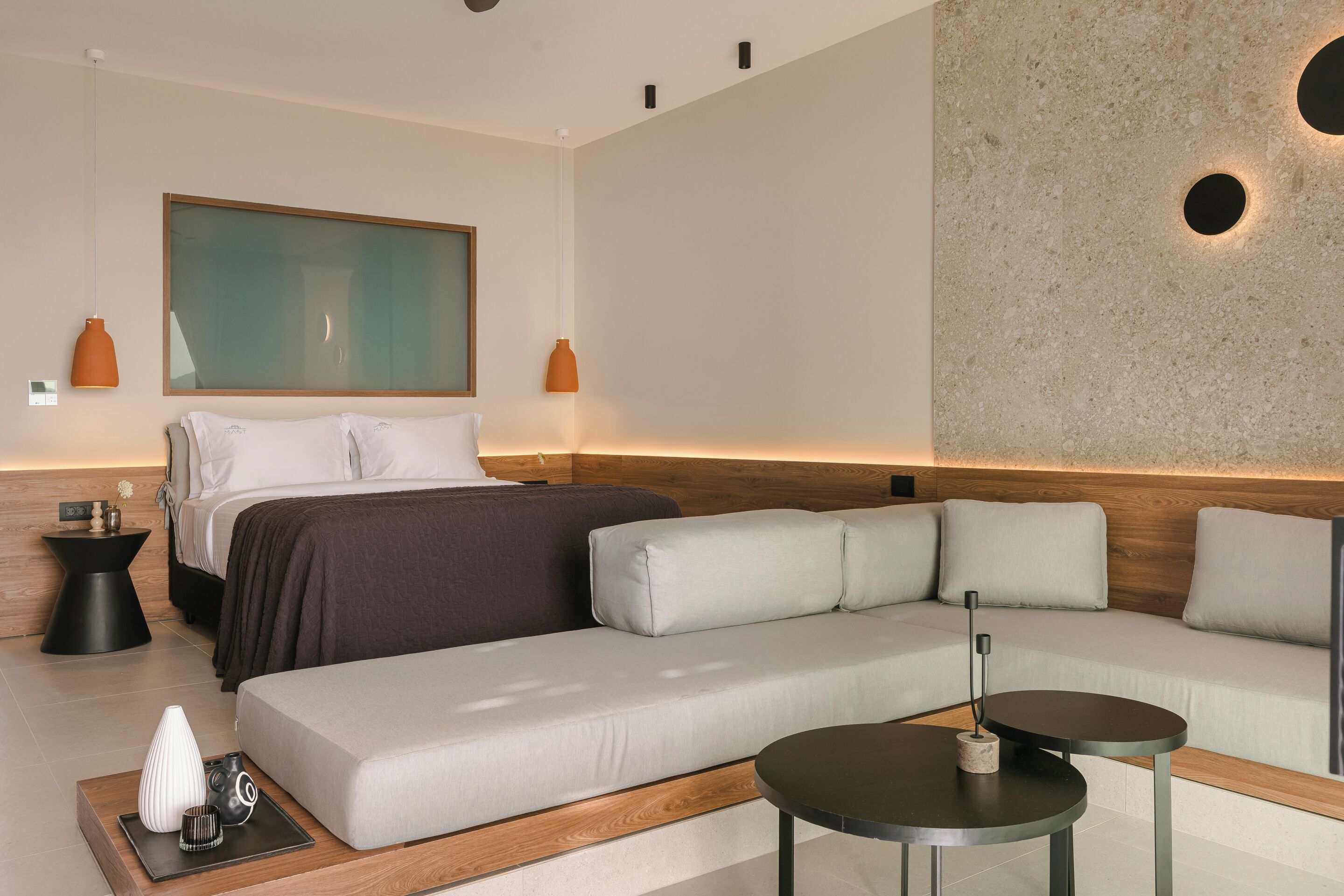 A modern hotel room with a bed, a sofa, a coffee table, and a large window.