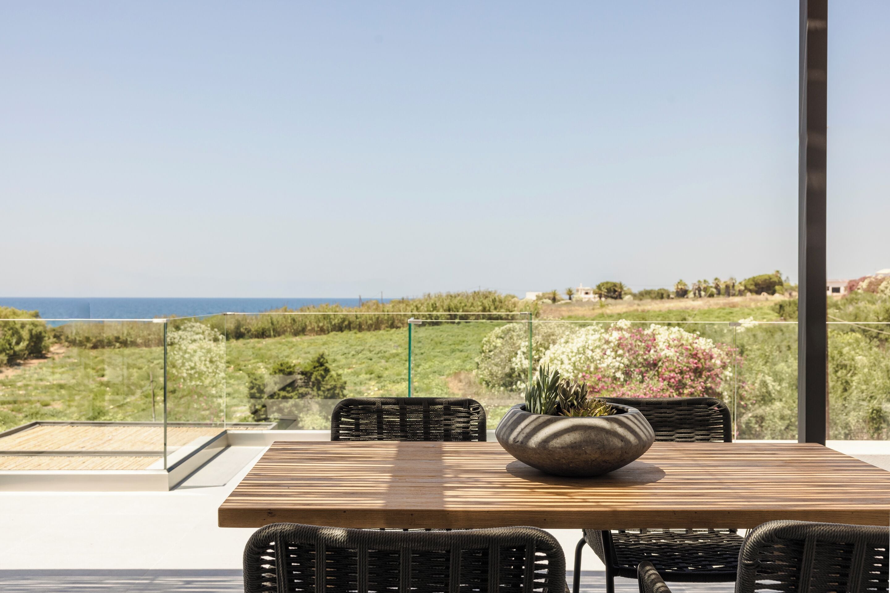 Una mesa de madera con sillas de mimbre en un balcón con vistas al paisaje costero.