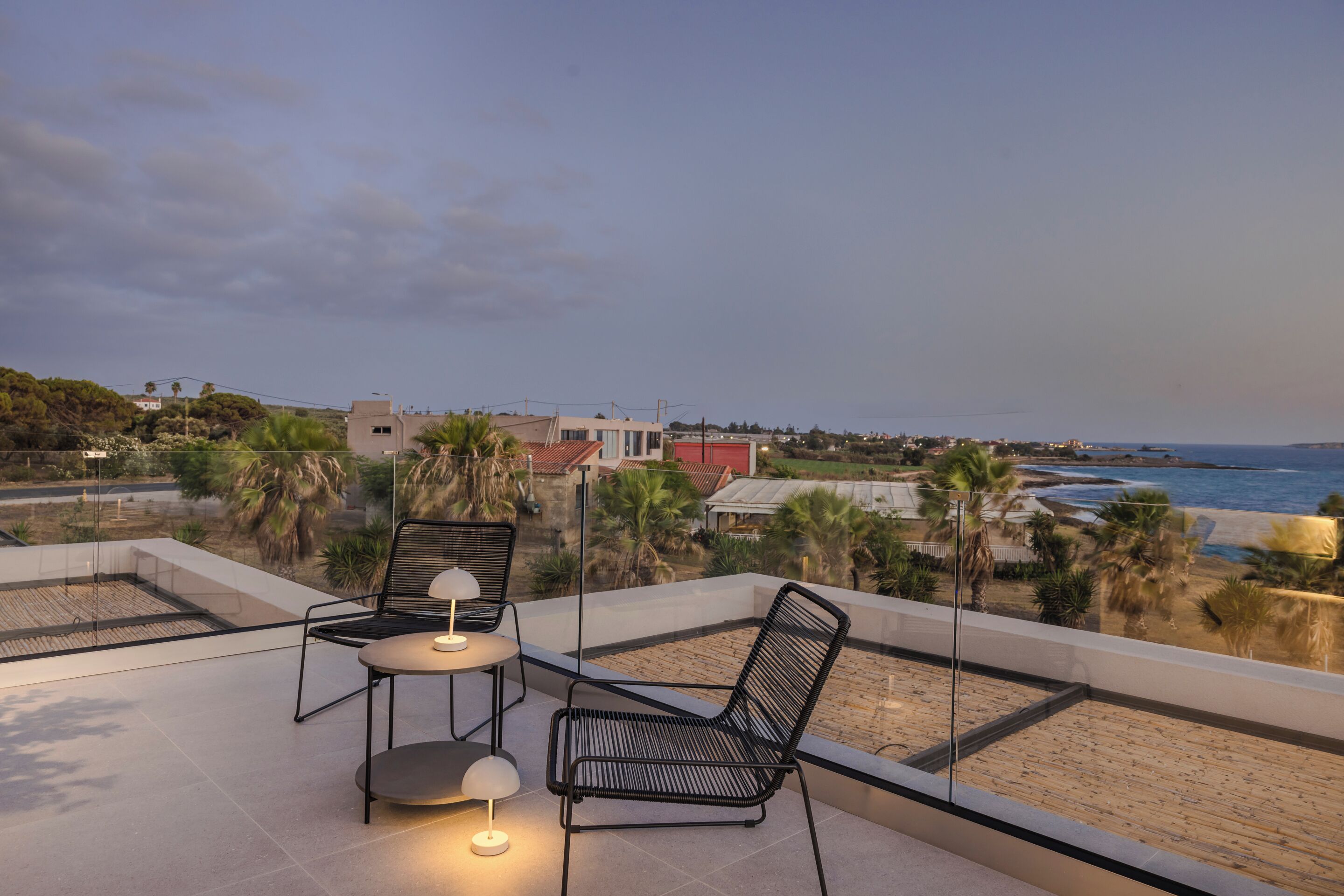 A rooftop terrace with two black metal chairs and a small table, overlooking a beach and a coastal town.