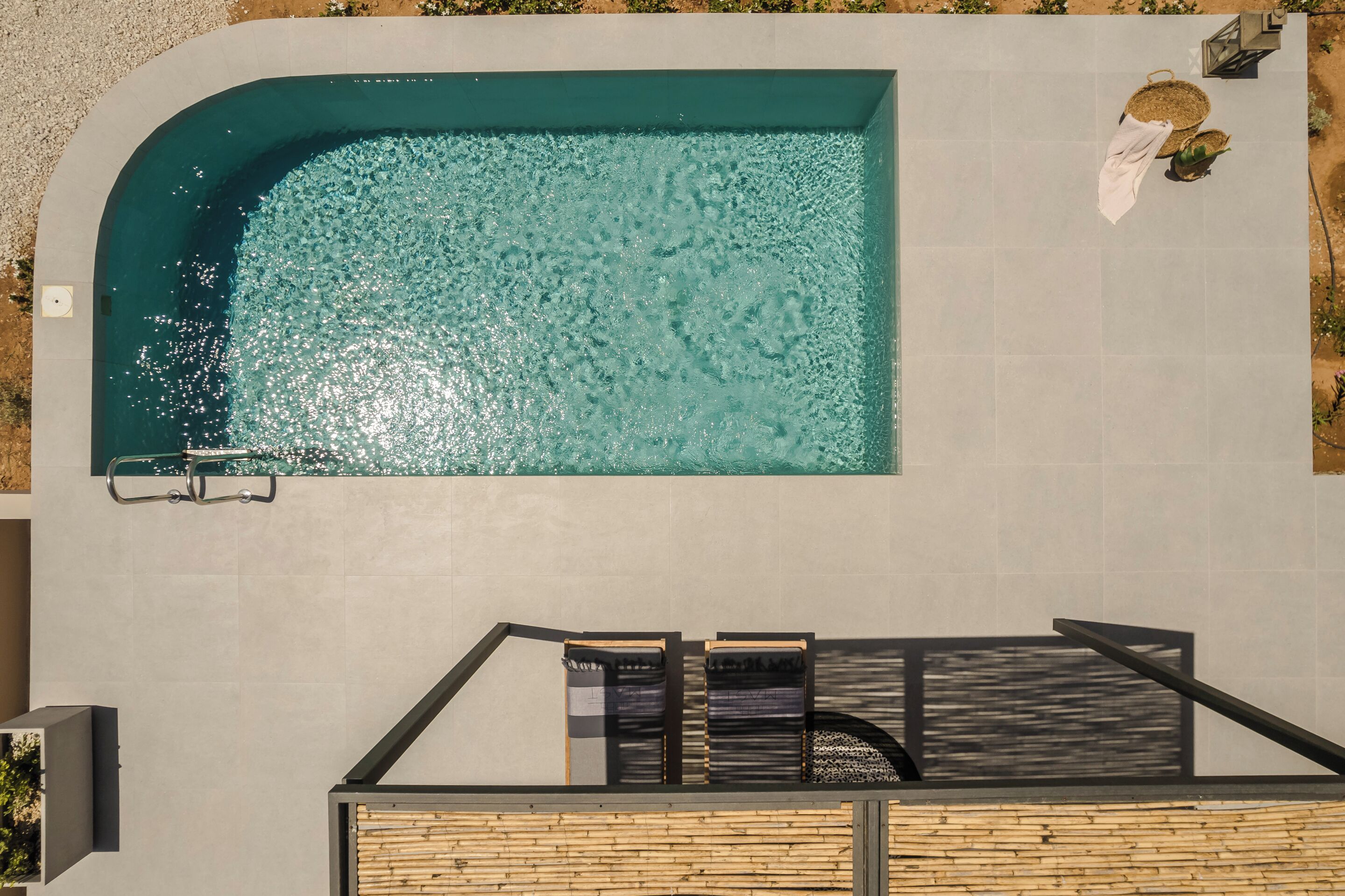 Ein Luftbild von einem Schwimmbecken mit Holzterrasse und Liegestühlen.