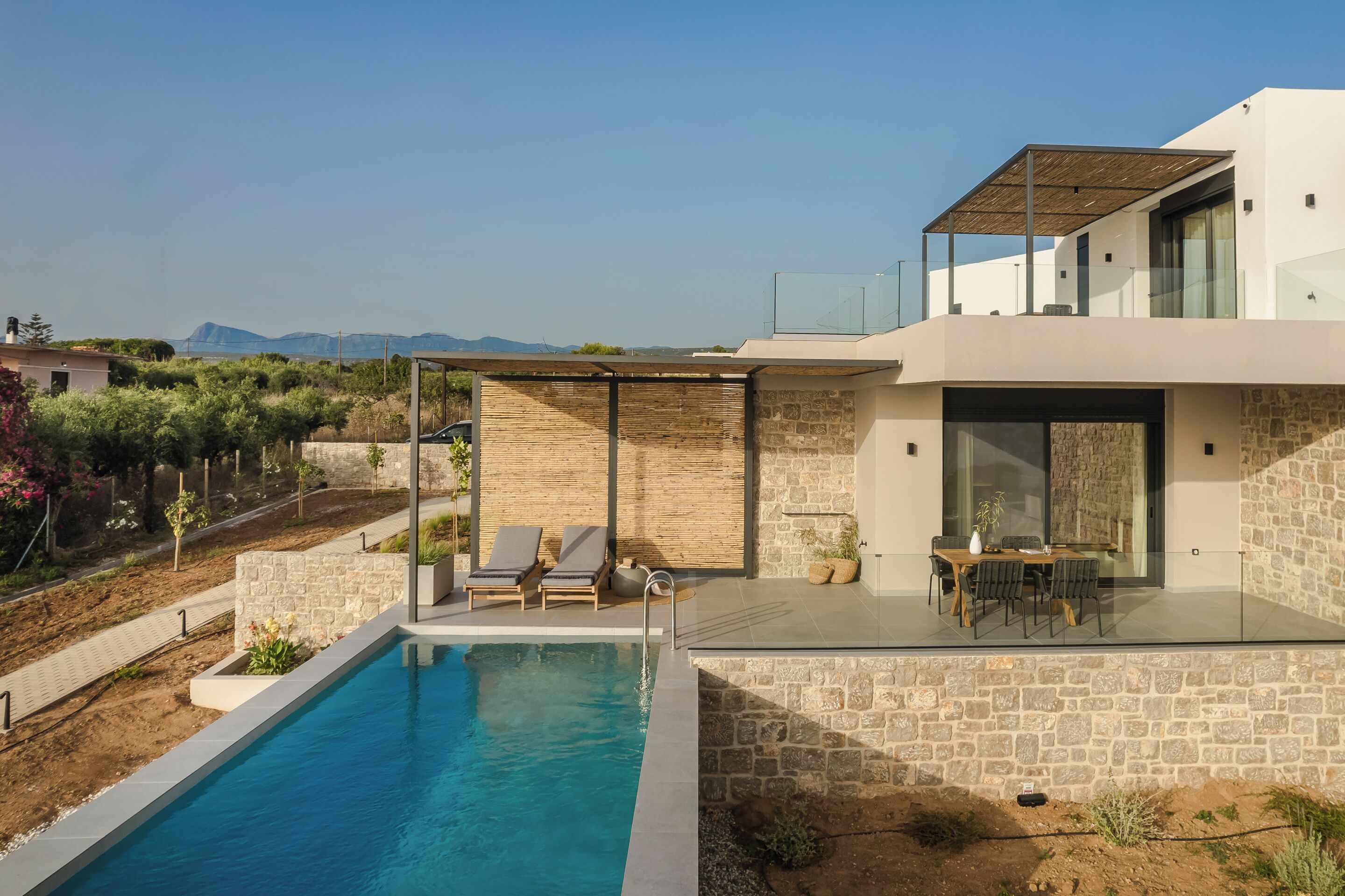 A modern house with a swimming pool, outdoor seating, and a view of the mountains.