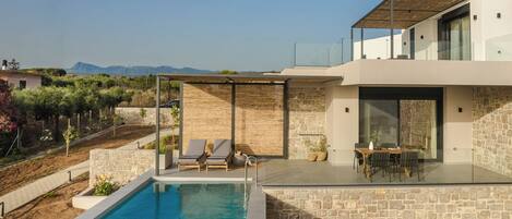 A modern house with a swimming pool, outdoor seating, and a view of the mountains.