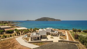 Una villa moderna con terraza en la azotea, piscina y vistas al mar y una pequeña isla.