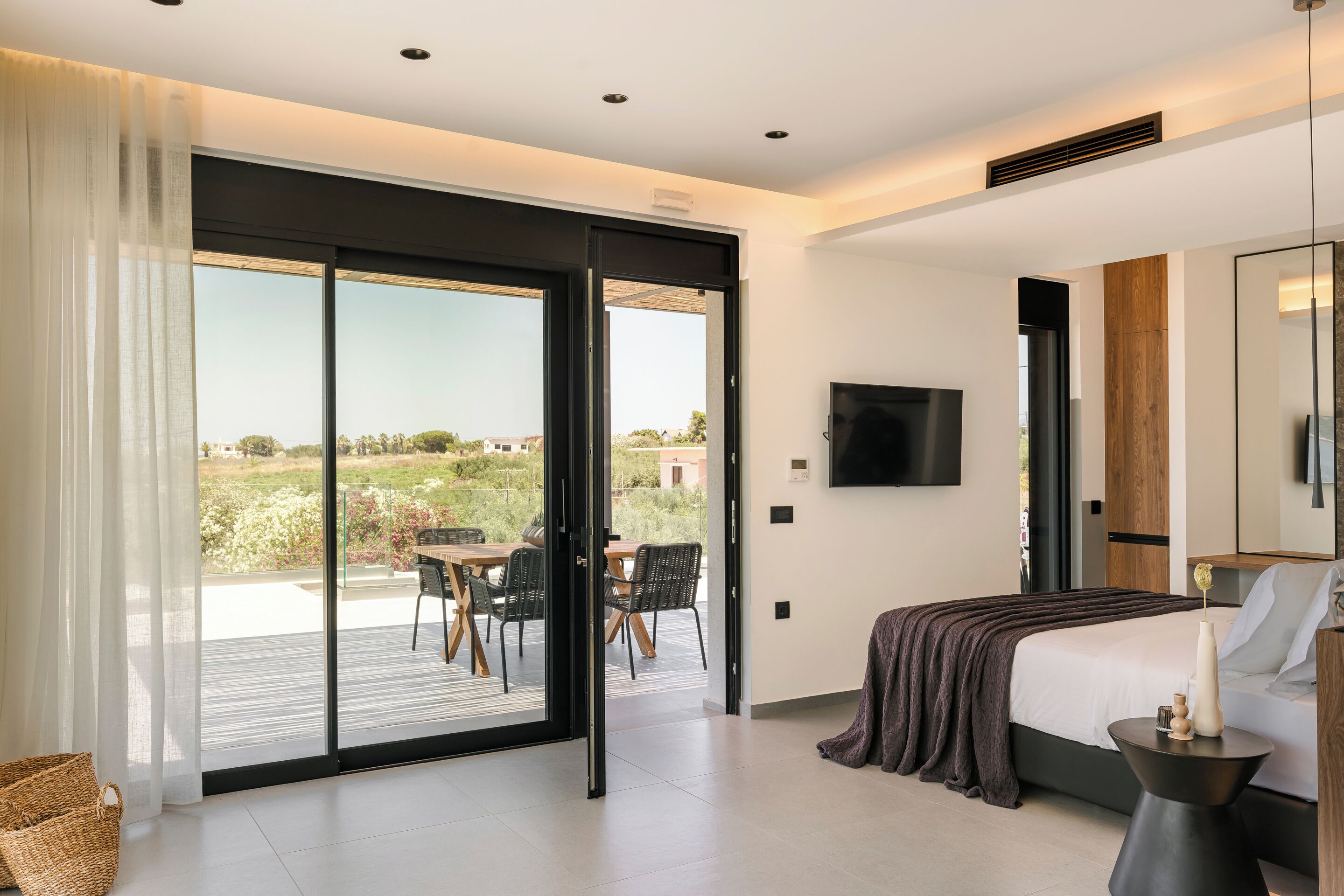 A modern bedroom with a large bed, a TV, and a balcony with outdoor seating.