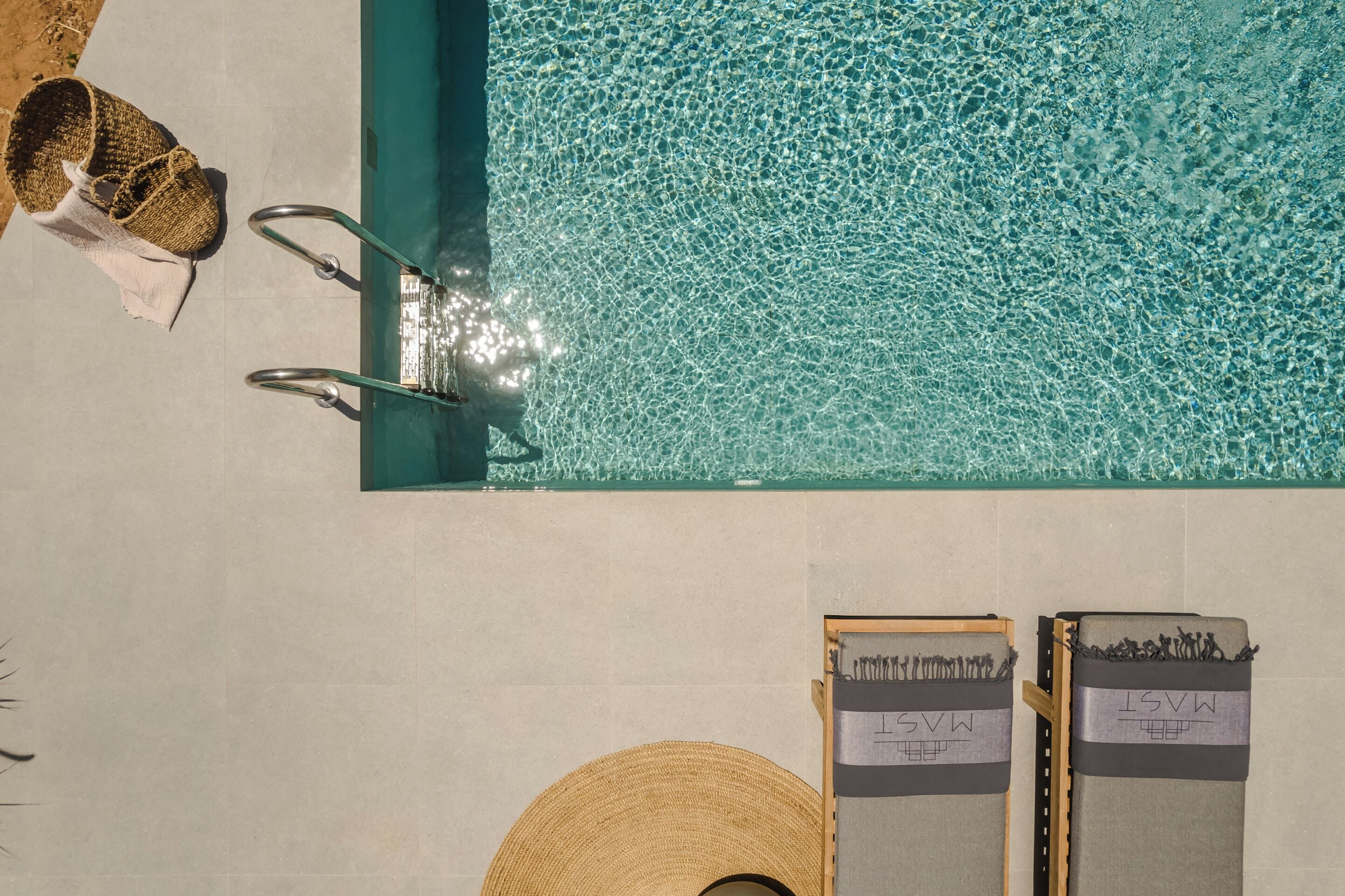 A swimming pool with clear water, a towel, and a hat on the edge.