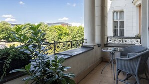 Un balcón con vistas a árboles y edificios, una mesita y sillas de mimbre.