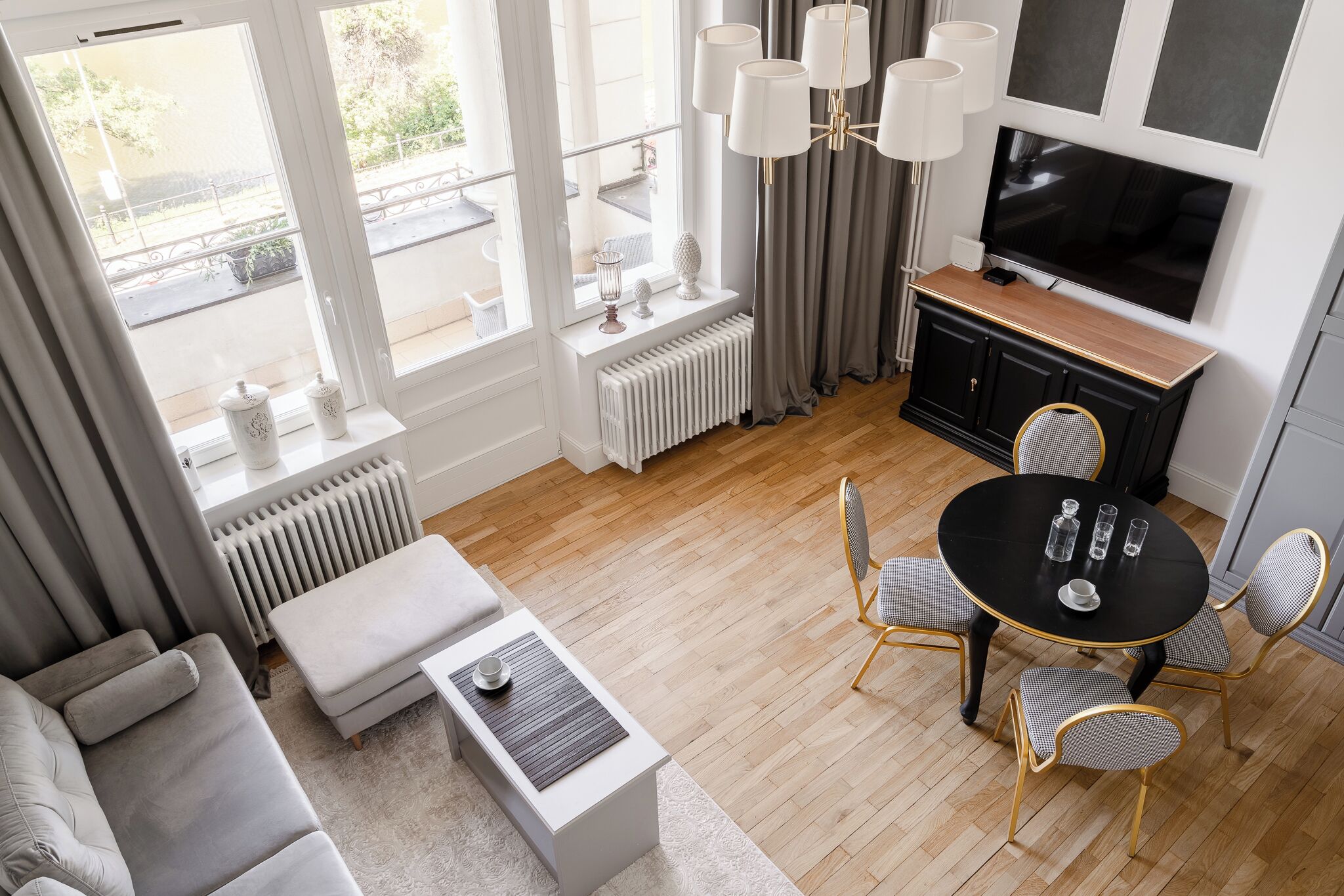 A modern living room with a sofa, ottoman, dining table with chairs, a TV, and a radiator.