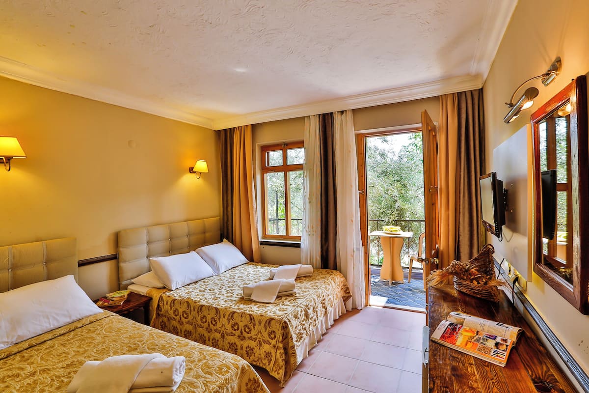 A hotel room with two beds, a small table, a television, and a window with curtains.