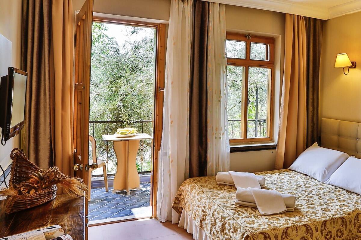 A hotel room with a bed, a small table, a TV, and a balcony with curtains.