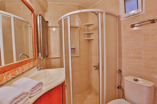 A bathroom with a curved shower enclosure, a sink with a mirror, and a toilet. - Club Hotel Gültur (Ayvacik)