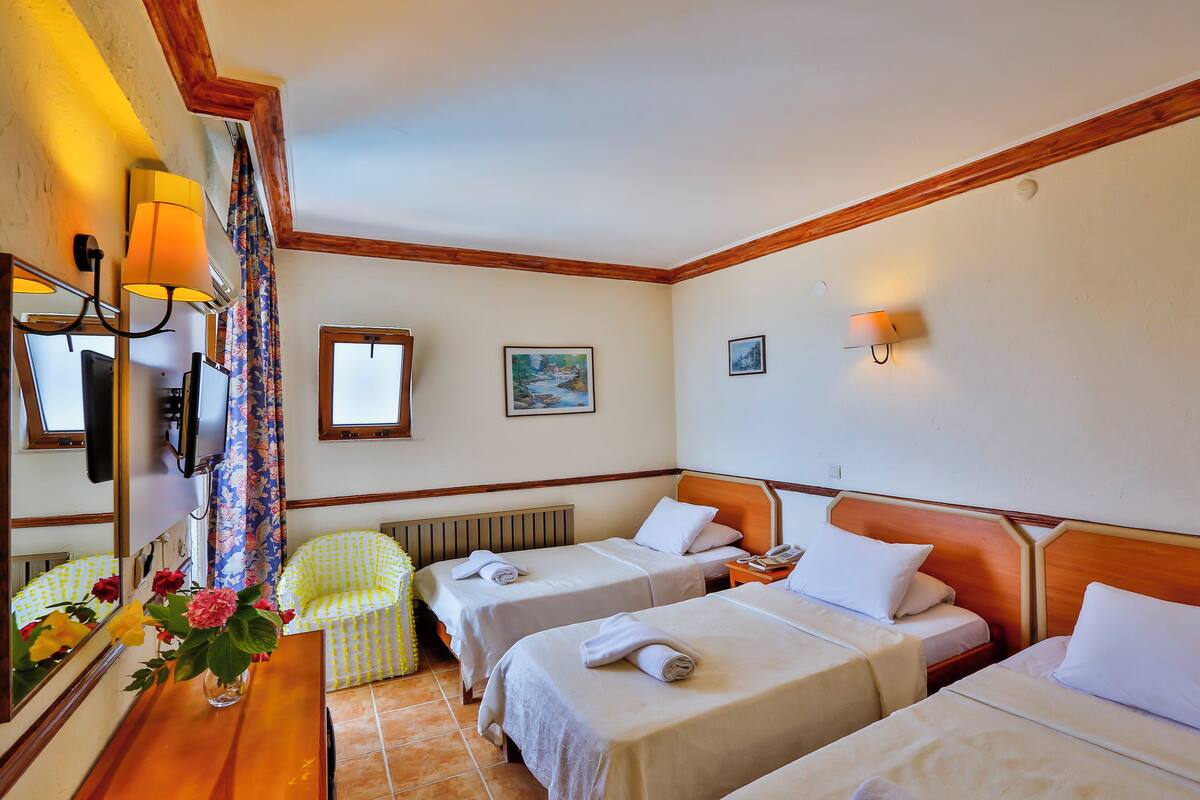 A hotel room with two single beds, a wooden headboard, a small table with a vase of flowers, a chair, and a mirror.