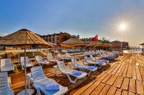 Ein Strandbereich mit Reihen weißer Liegestühle und strohgedeckten Sonnenschirmen, typisch für eine luxuriöse Ferienanlage.