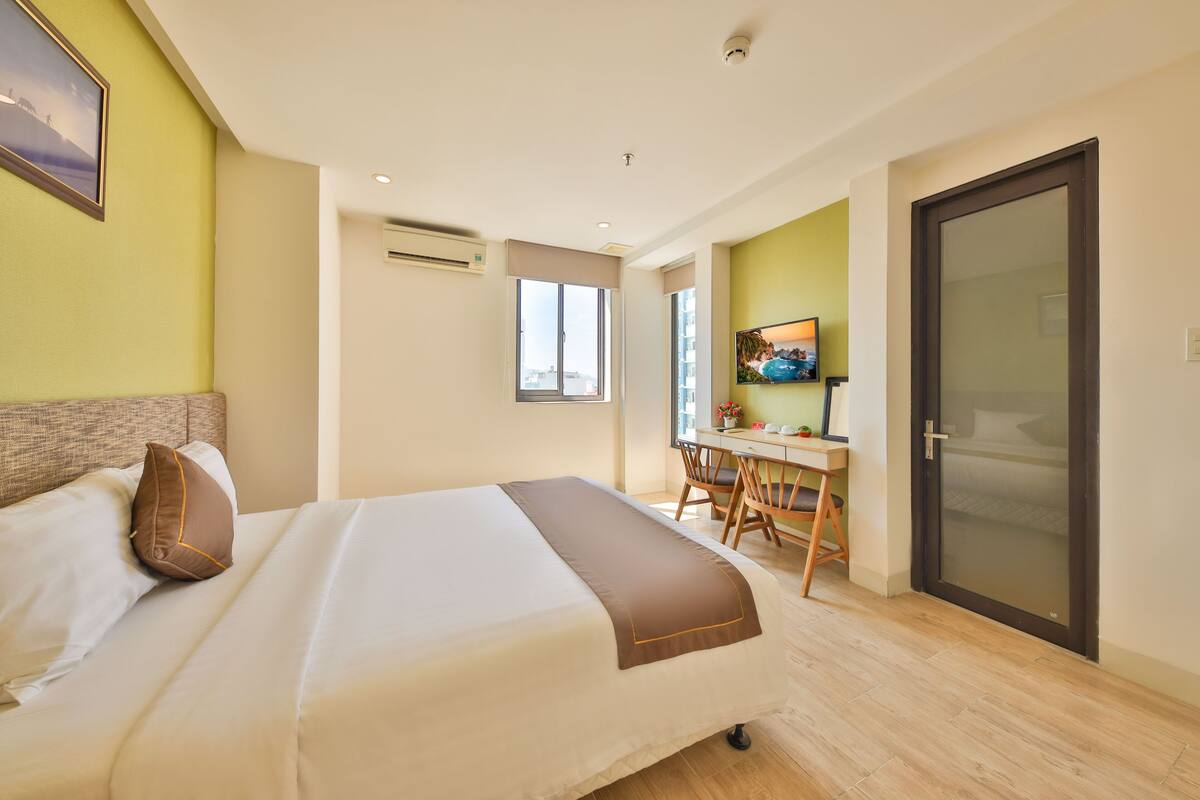 A modern hotel room with a large bed, a desk, and a door.
