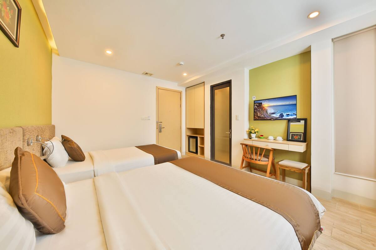A hotel room with two beds, a desk, a chair, and a television.