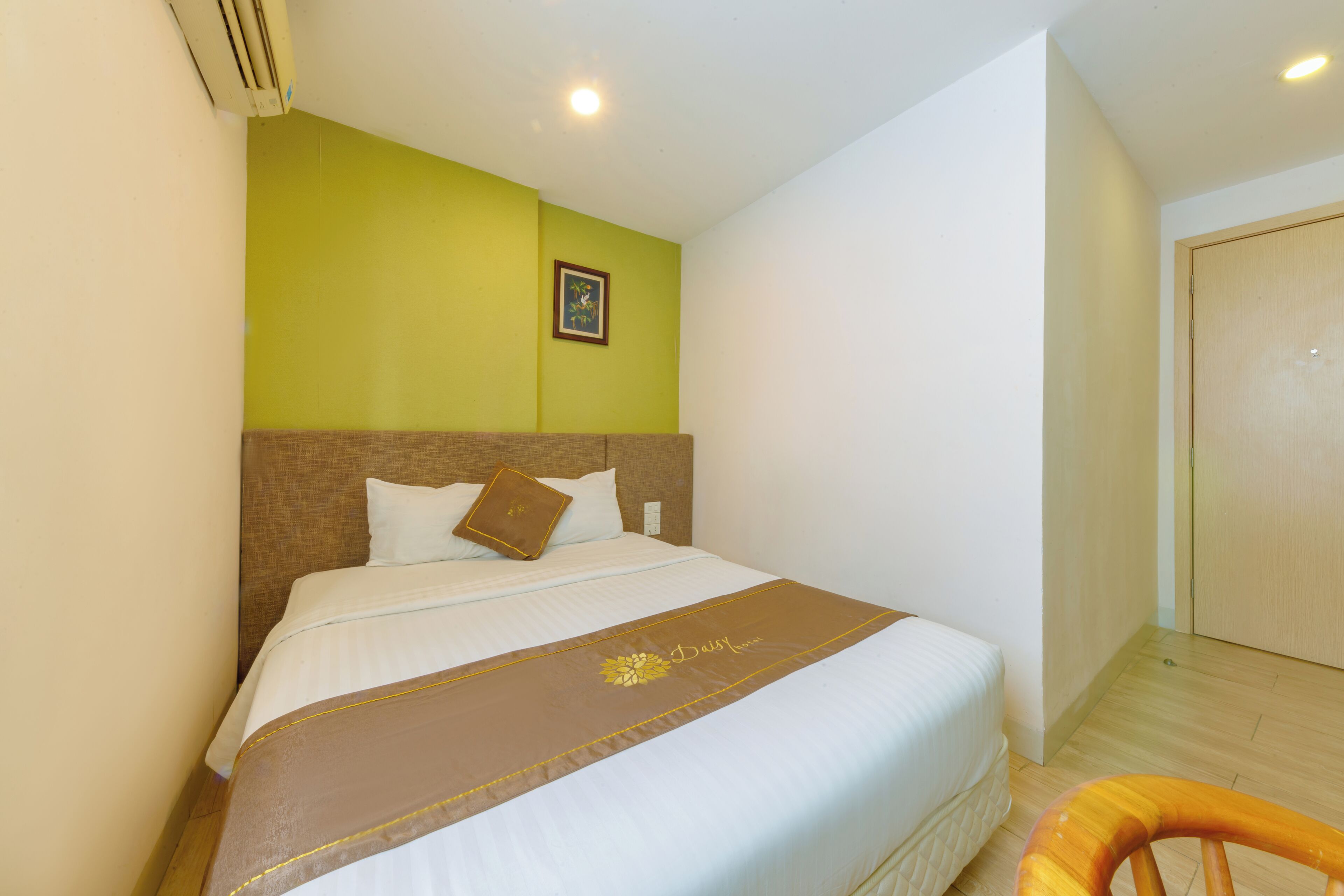 A hotel room with a bed, a wooden headboard, a green accent wall, a framed picture, and a wooden door.