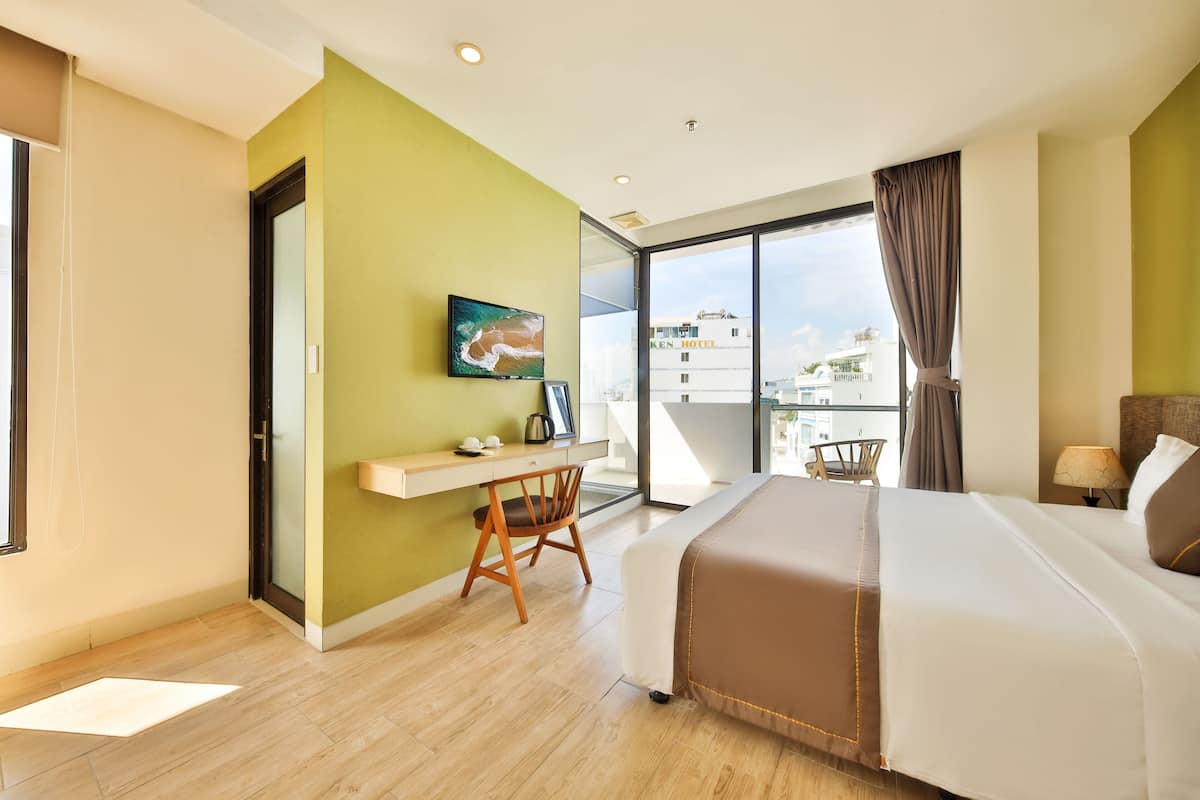 A modern hotel room with a bed, desk, chair, and a large window offering a city view.