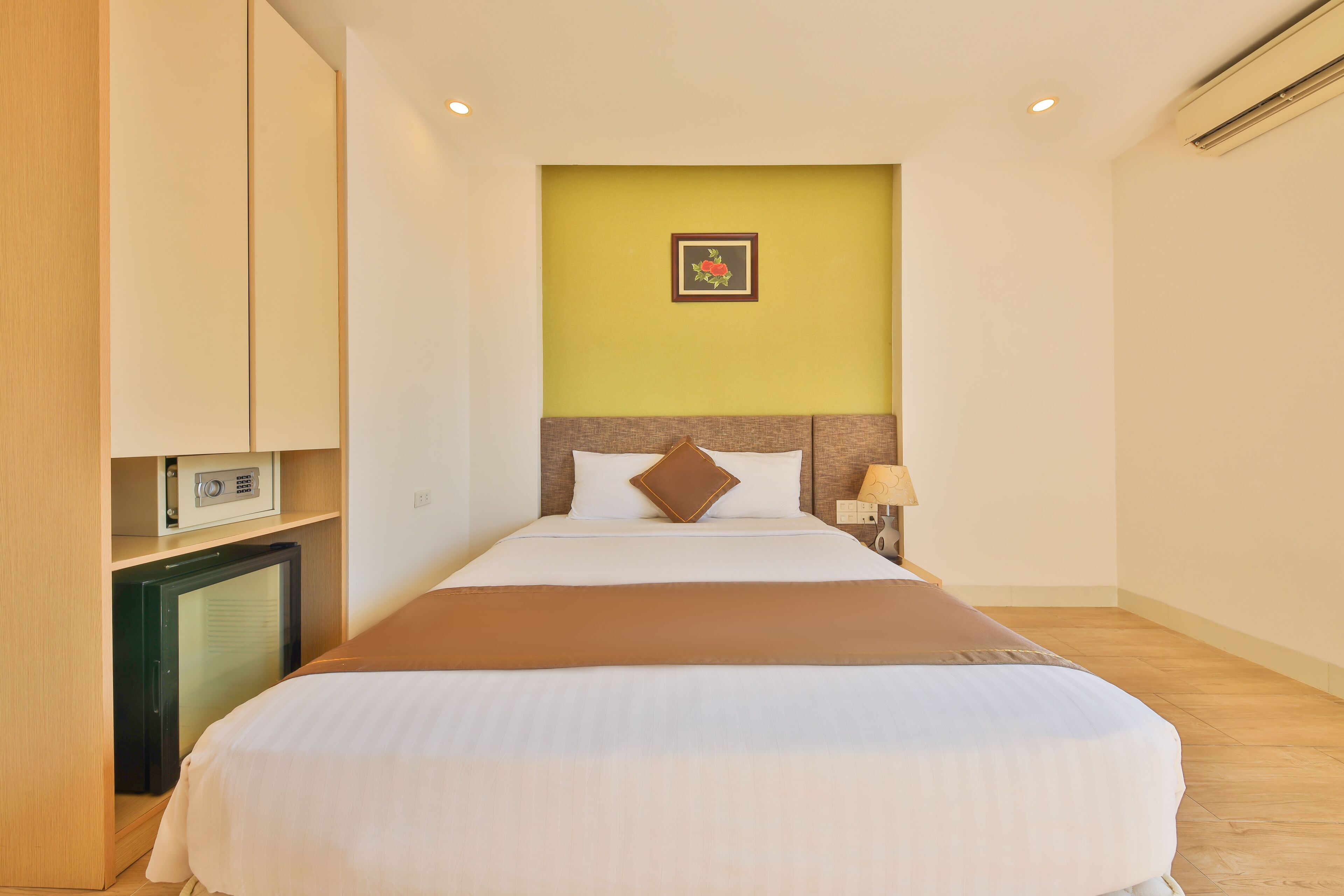 A hotel room with a bed, a bedside table with a lamp, a small TV, and a picture on the wall.